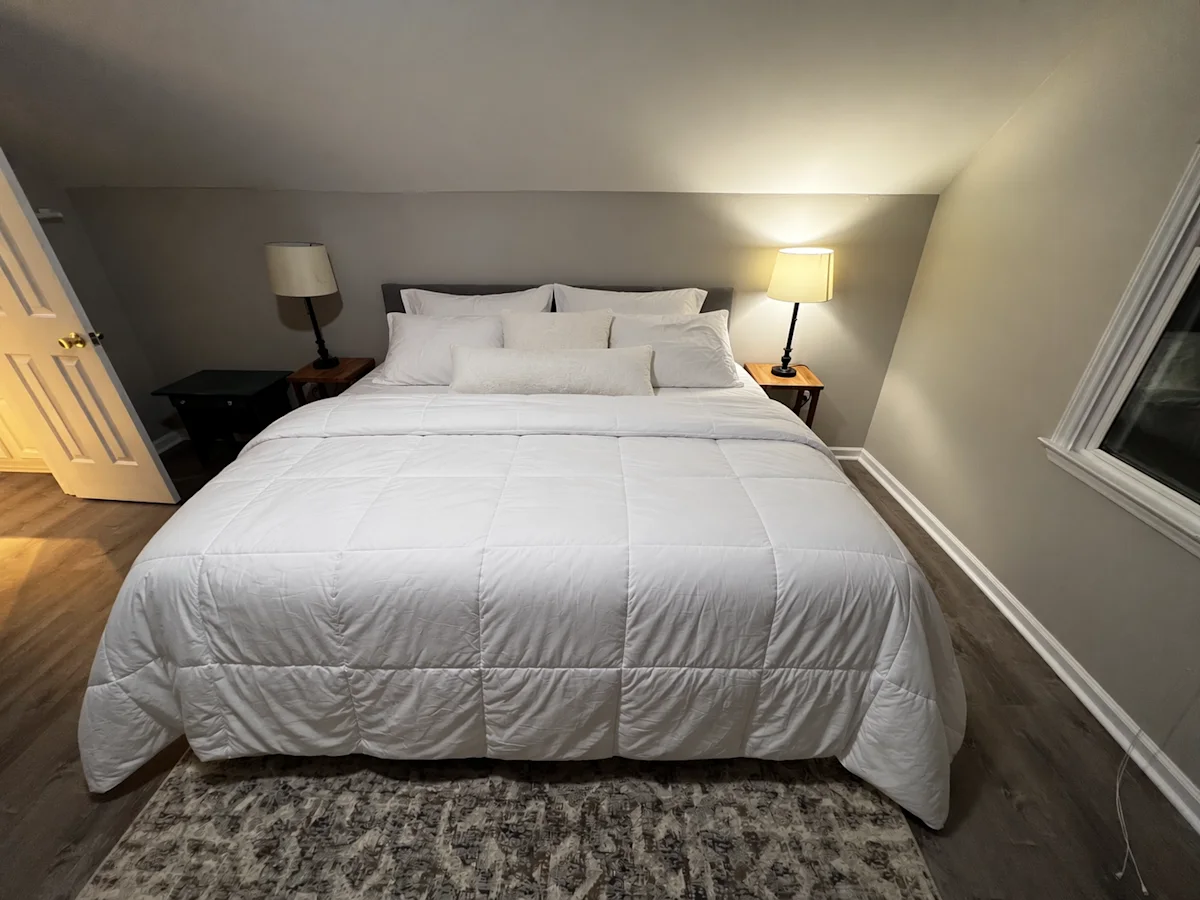 Edited result: the same bedroom with the bed neatly made and pillows arranged.