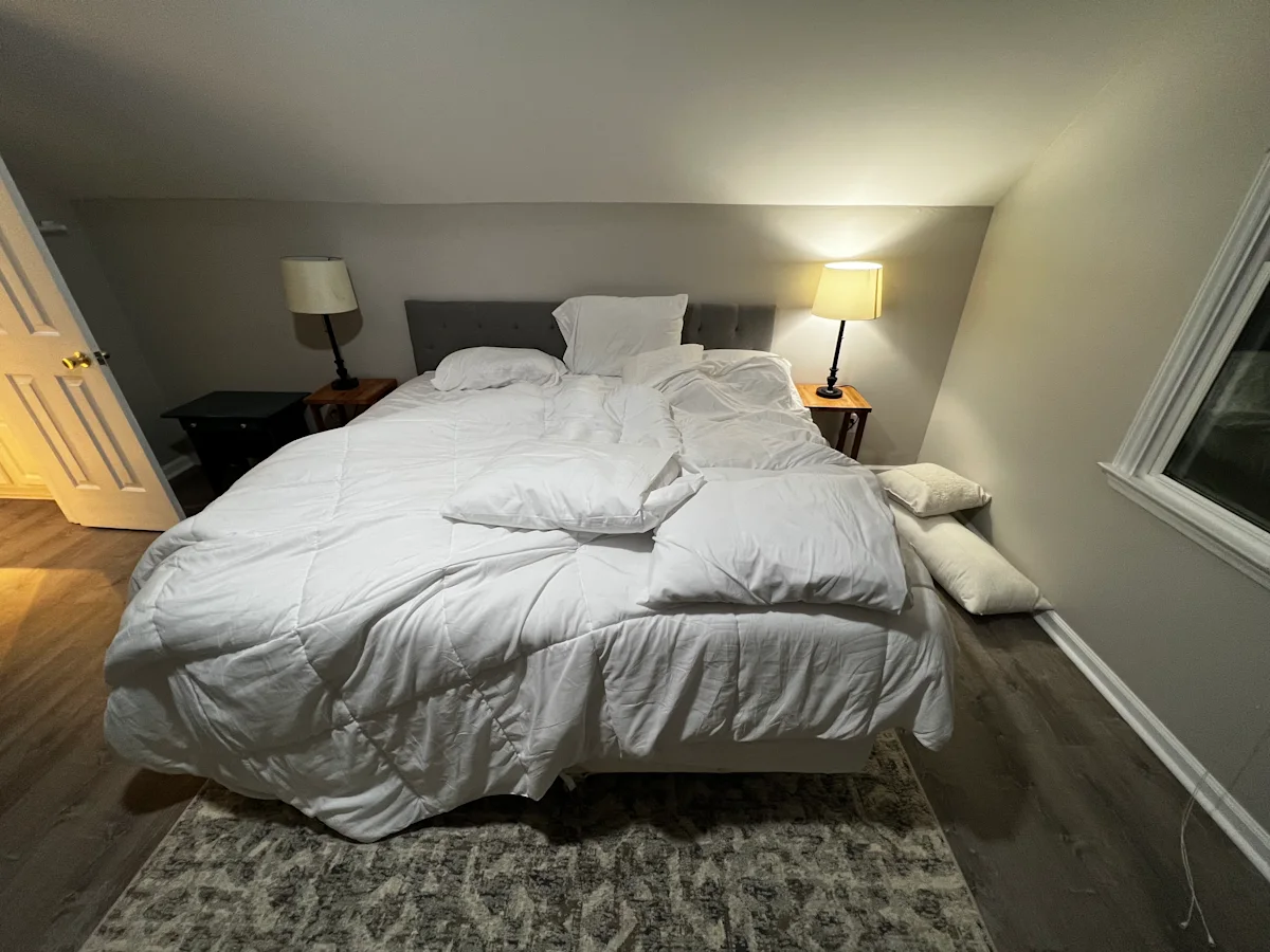 Reference photo: an unmade bed with rumpled white bedding and scattered pillows.